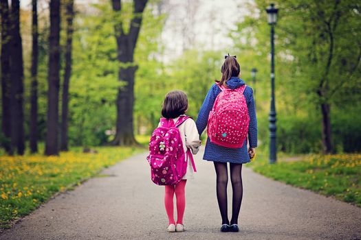 Two sisters are going to the school pass throught the local park.