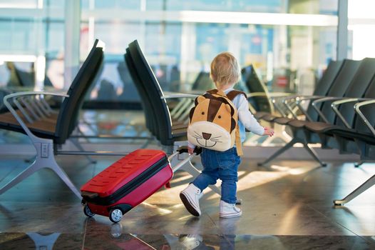 Kid travelling through the airport with suitcase and toys